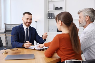 Photo of Couple having meeting with professional notary at wooden desk indoors