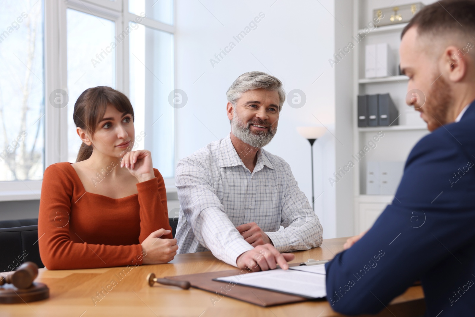 Photo of Couple having meeting with professional notary at wooden desk indoors