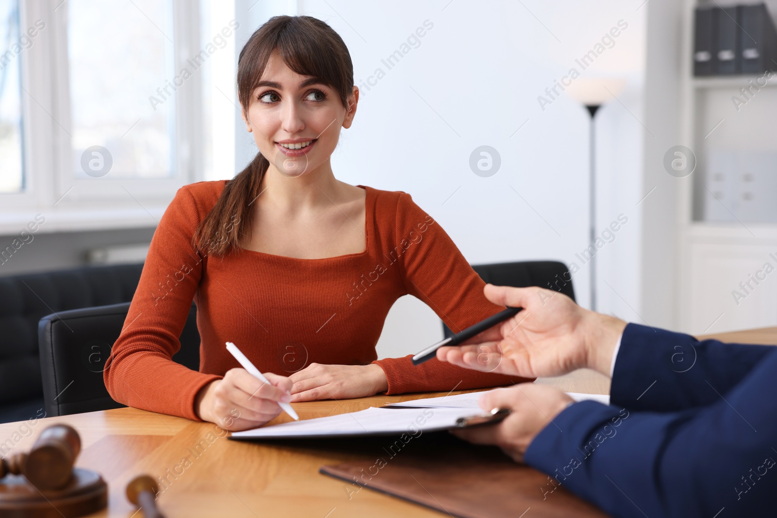 Photo of Client signing notarial paperwork during meeting with lawyer at wooden desk indoors