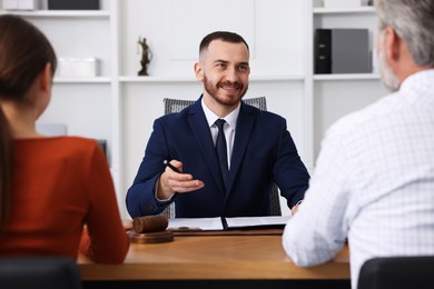 Photo of Man and woman having meeting with professional notary at wooden desk indoors