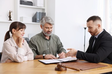 Photo of Clients signing notarial paperwork during meeting with lawyer at wooden desk indoors