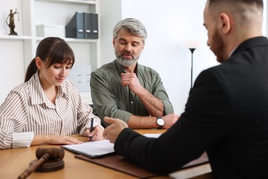 Photo of Clients signing notarial paperwork during meeting with lawyer at wooden desk indoors