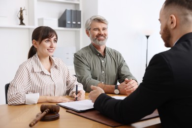 Clients signing notarial paperwork during meeting with lawyer at wooden desk indoors