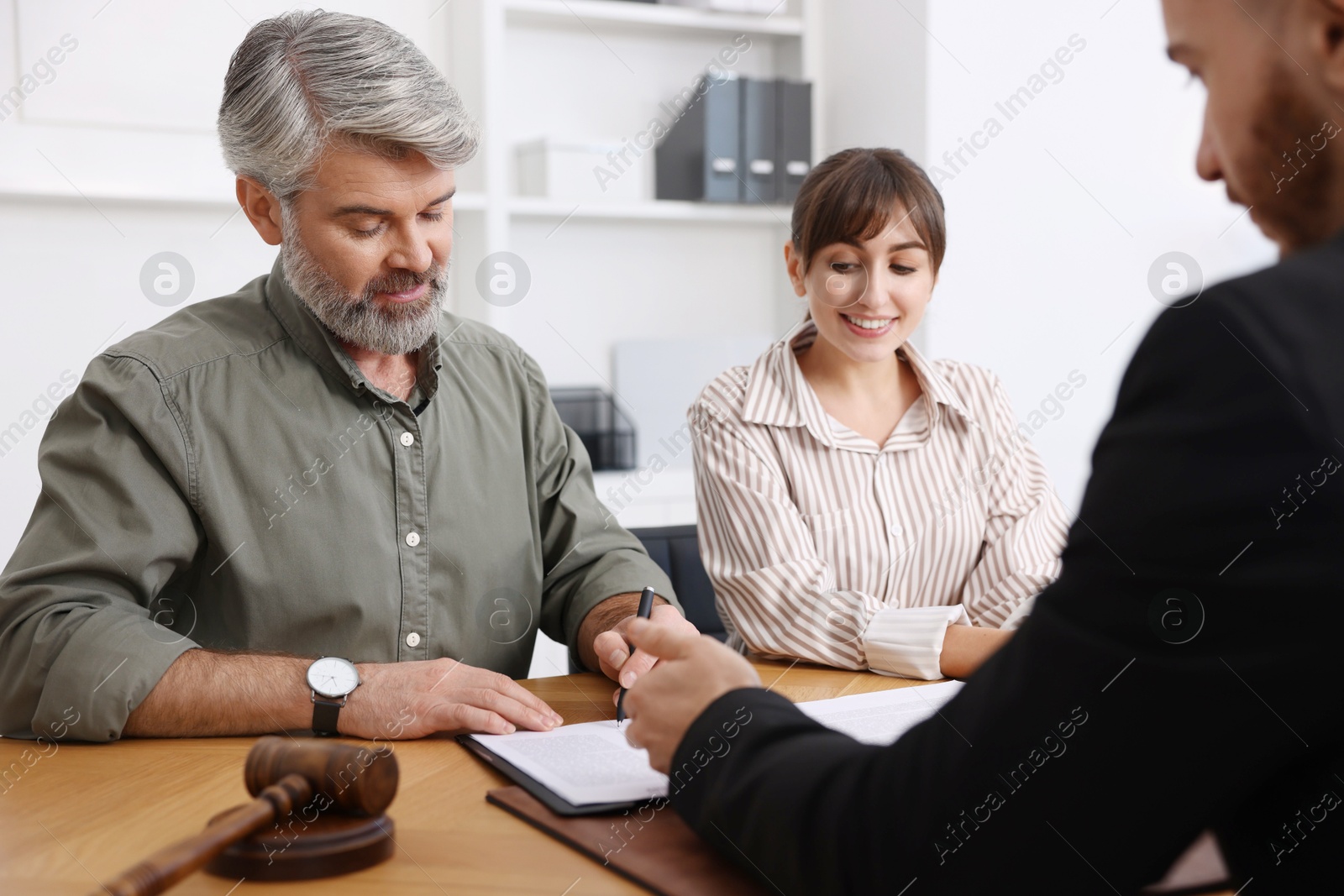 Photo of Clients signing notarial paperwork during meeting with lawyer at wooden desk indoors