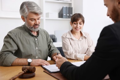 Photo of Clients signing notarial paperwork during meeting with lawyer at wooden desk indoors