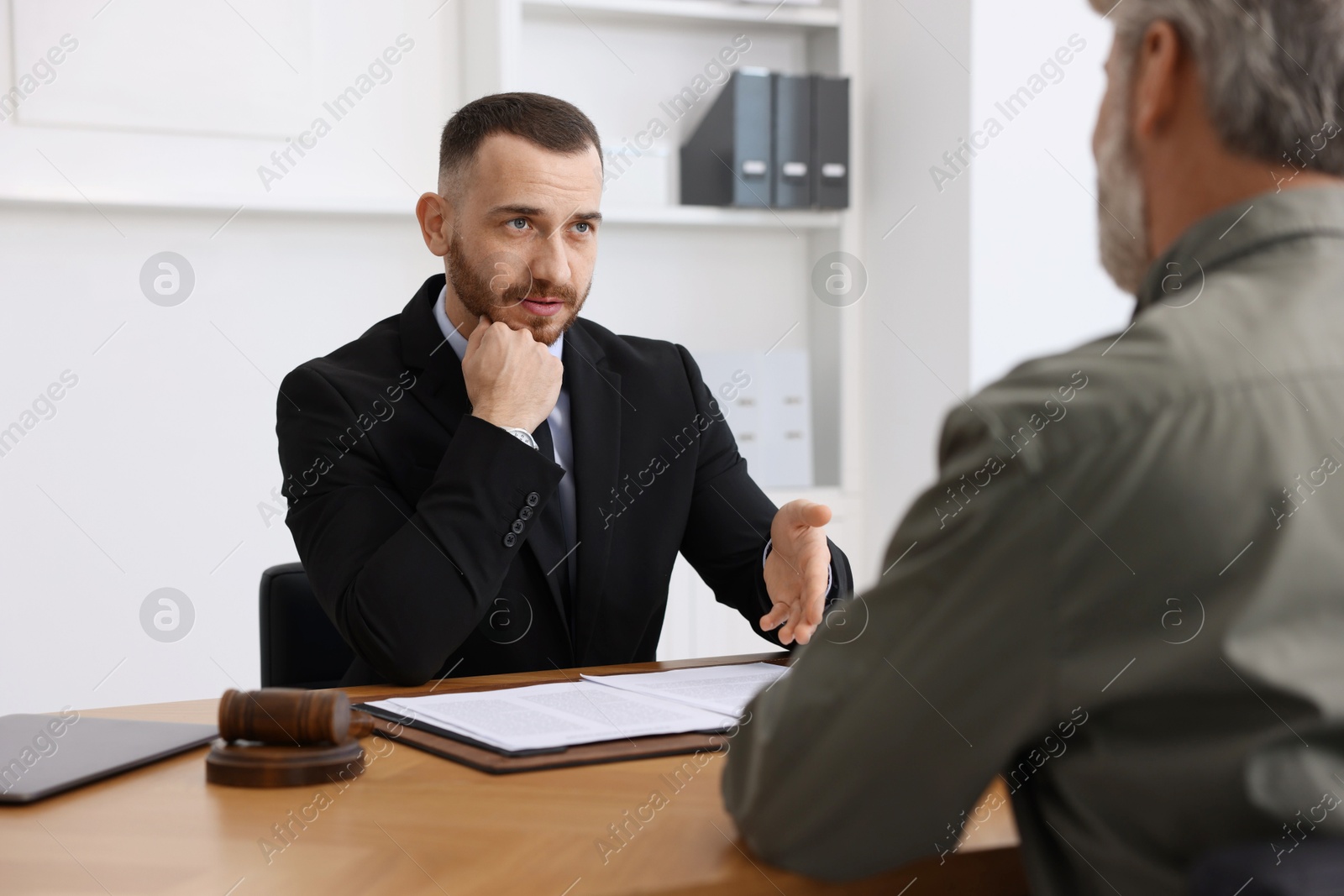 Photo of Man having meeting with professional lawyer at wooden desk indoors