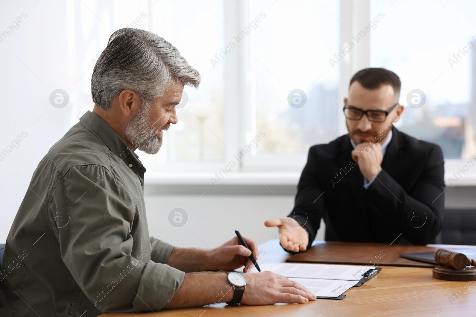 Photo of Client signing notarial paperwork during meeting with lawyer at wooden desk indoors, selective focus