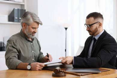 Client signing notarial paperwork during meeting with lawyer at wooden desk indoors