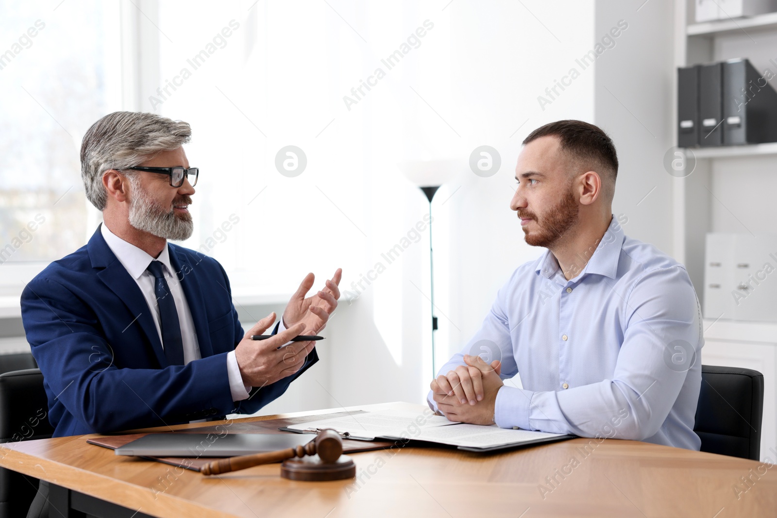 Photo of Man having meeting with professional lawyer at wooden desk indoors