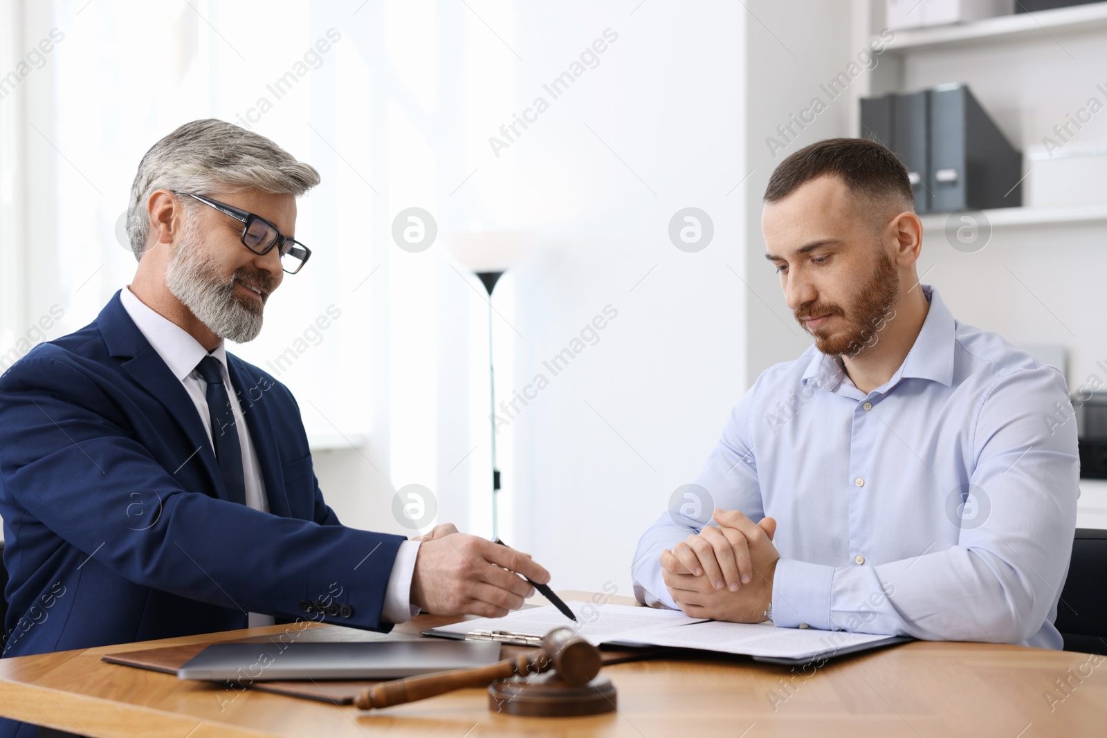 Photo of Man having meeting with professional lawyer at wooden desk indoors