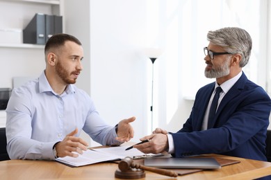 Man having meeting with professional lawyer at wooden desk indoors