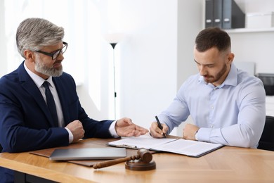 Photo of Client signing notarial paperwork during meeting with lawyer at wooden desk indoors