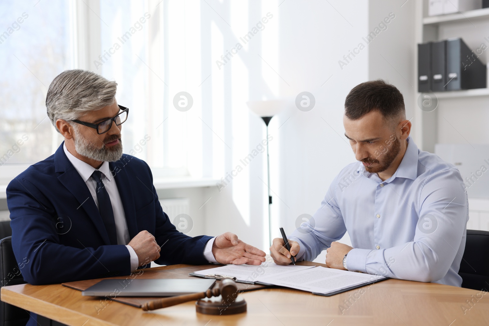 Photo of Client signing notarial paperwork during meeting with lawyer at wooden desk indoors