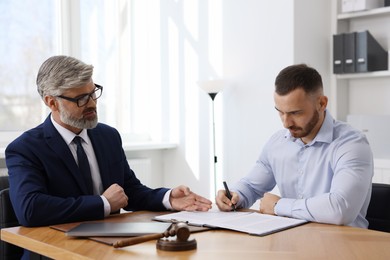 Client signing notarial paperwork during meeting with lawyer at wooden desk indoors