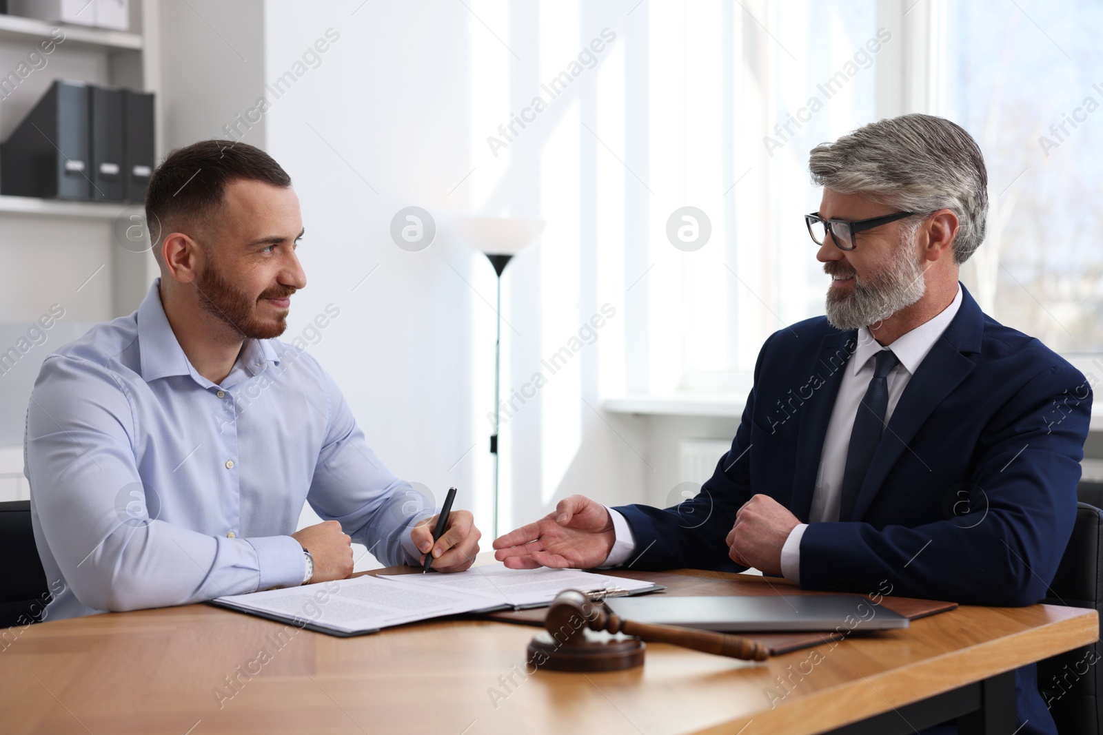 Photo of Client signing notarial paperwork during meeting with lawyer at wooden desk indoors