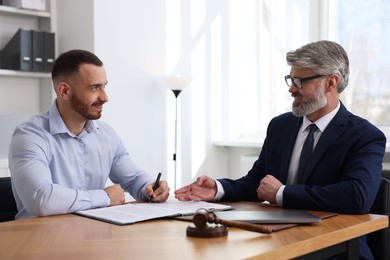 Client signing notarial paperwork during meeting with lawyer at wooden desk indoors