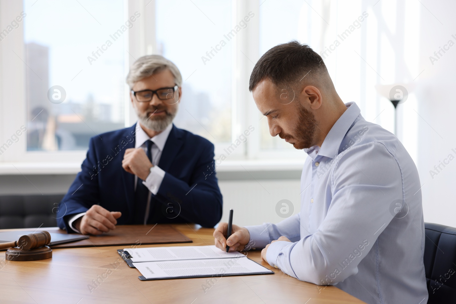 Photo of Client signing notarial paperwork during meeting with lawyer at wooden desk indoors, selective focus