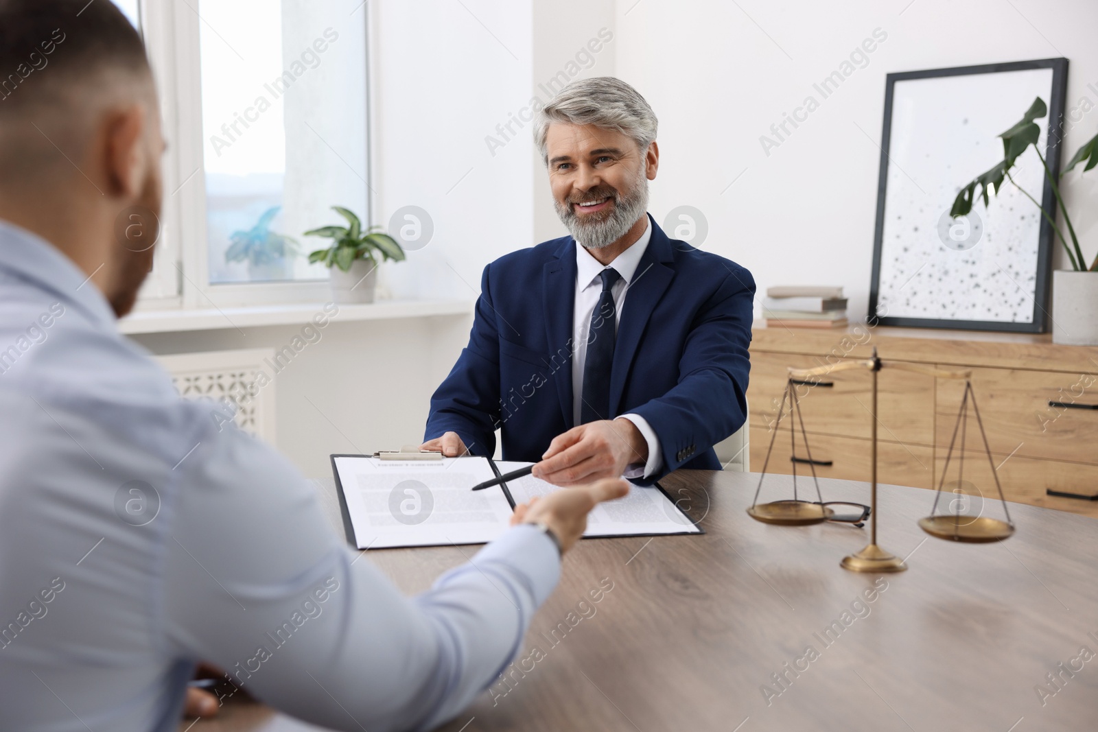 Photo of Client signing notarial paperwork during meeting with lawyer at wooden desk indoors