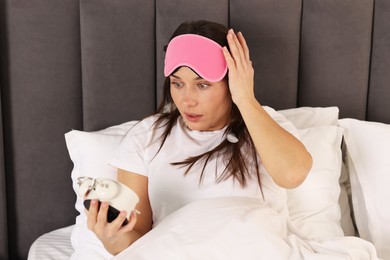 Overslept woman with alarm clock in bed at home