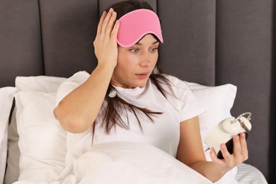 Overslept woman with alarm clock in bed at home