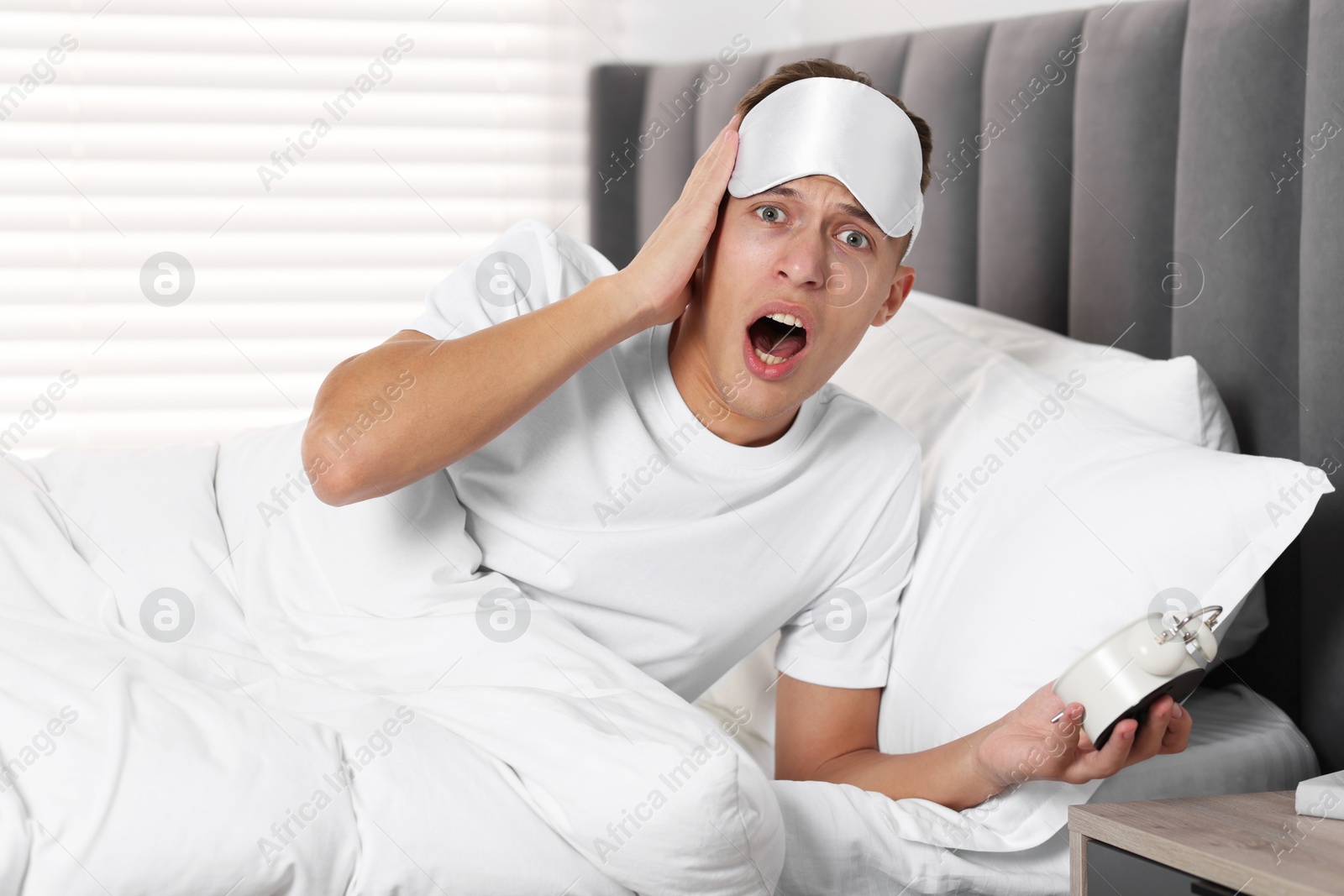 Photo of Overslept man with alarm clock in bed at home