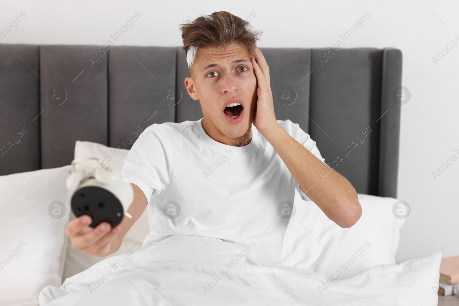 Photo of Overslept man with alarm clock in bed at home