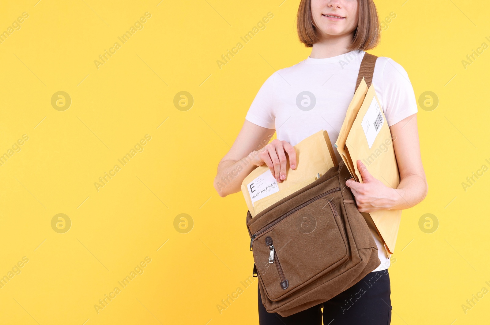 Photo of Happy postwoman with bag and envelopes on yellow background, closeup. Space for text