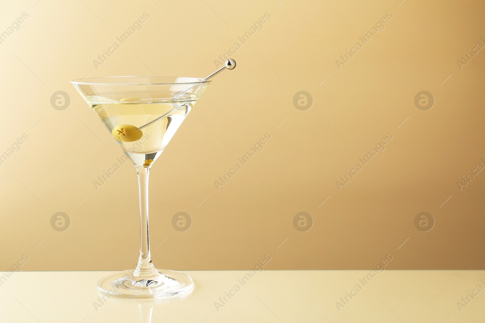 Photo of Martini cocktail with olive in glass on beige table, space for text