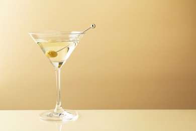 Photo of Martini cocktail with olive in glass on beige table, space for text