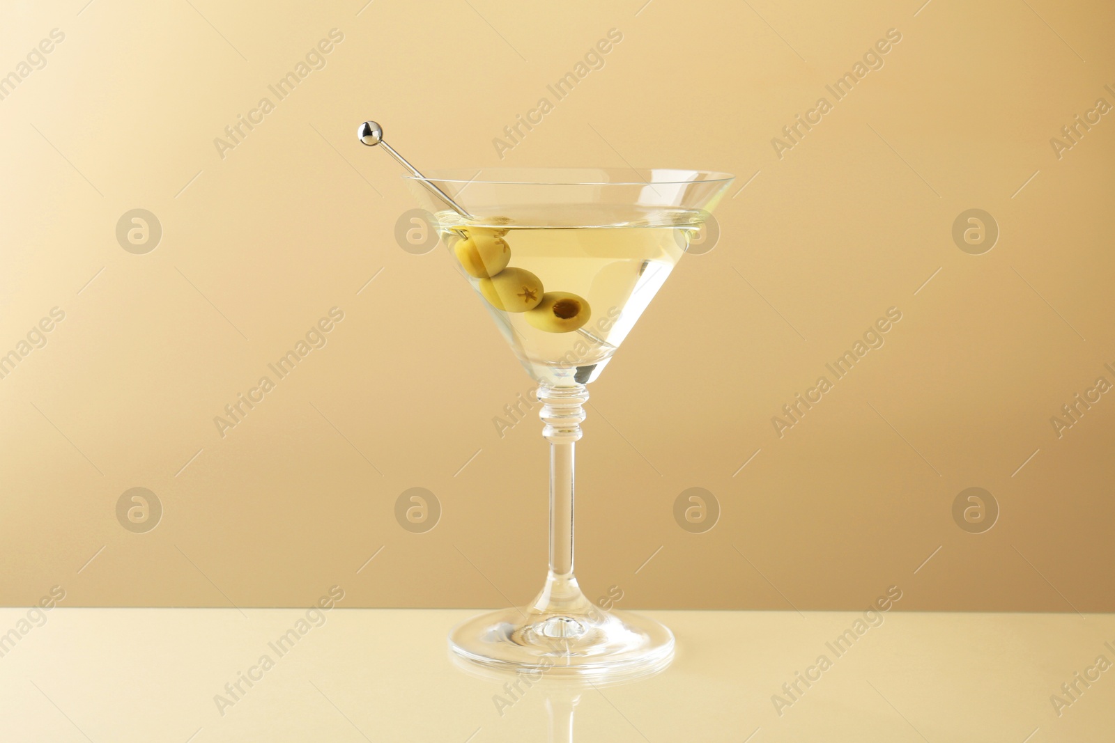 Photo of Martini cocktail with olives in glass on beige table