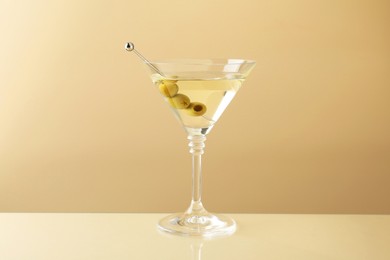 Photo of Martini cocktail with olives in glass on beige table