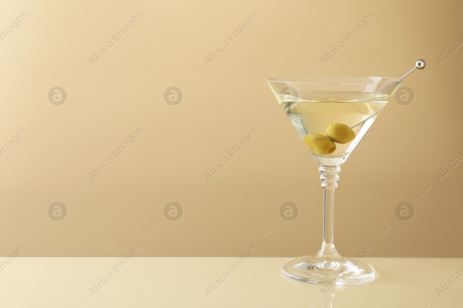 Photo of Martini cocktail with olives in glass on beige table, space for text