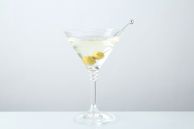 Photo of Martini cocktail with olives in glass on light grey table