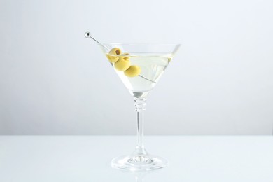 Photo of Martini cocktail with olives in glass on light table