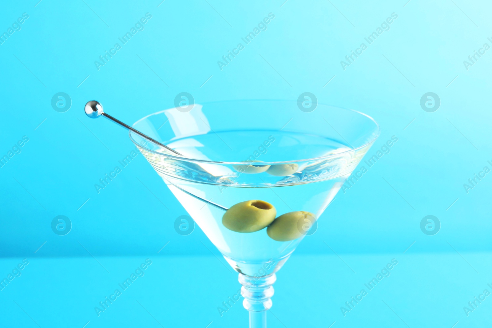 Photo of Martini cocktail with olives in glass on light blue background, closeup