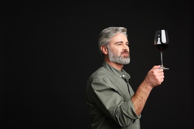 Professional sommelier analyzing quality of red wine on black background, space for text