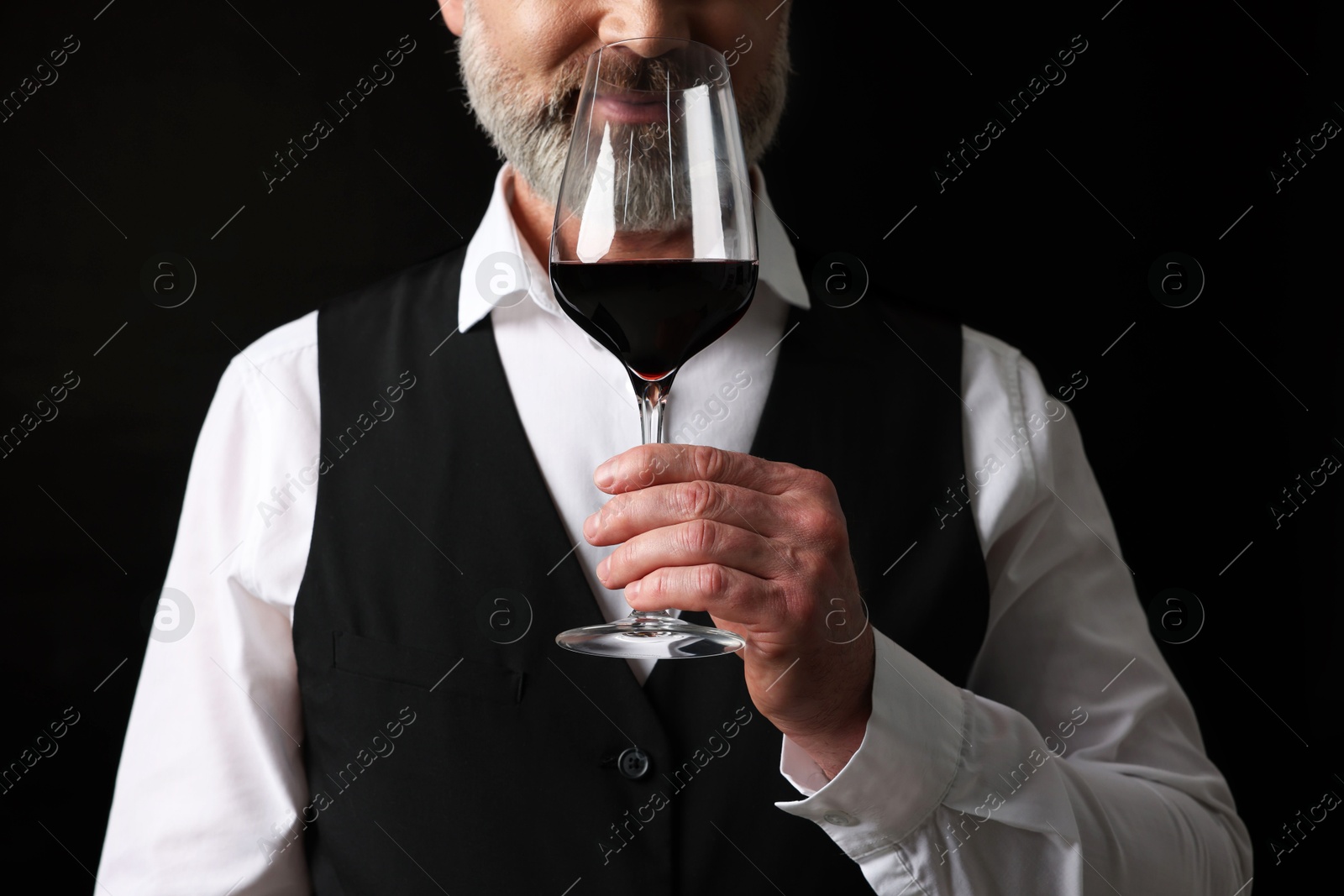 Photo of Professional sommelier tasting red wine on black background, closeup