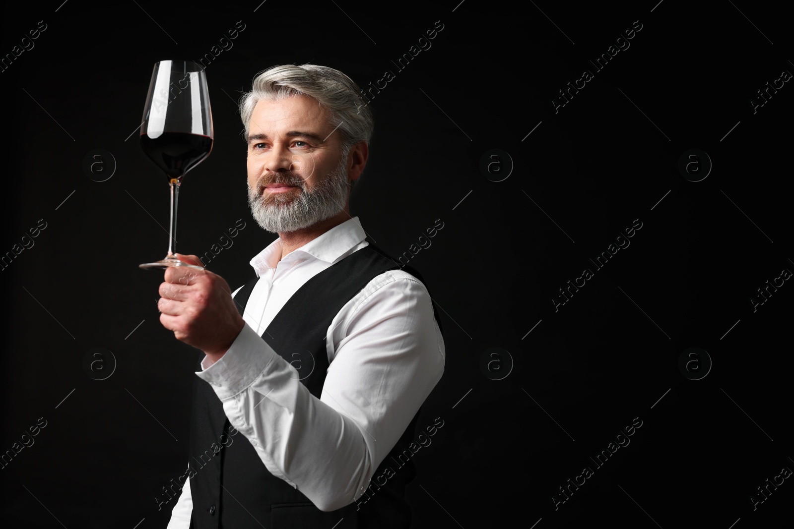 Photo of Professional sommelier analyzing quality of red wine on black background, space for text