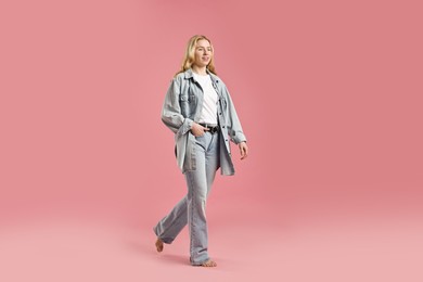 Photo of Smiling woman in stylish jeans on pink background