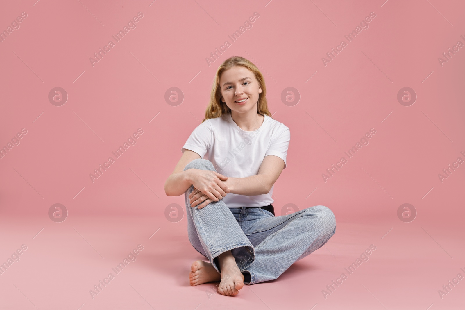 Photo of Smiling woman in stylish jeans on pink background