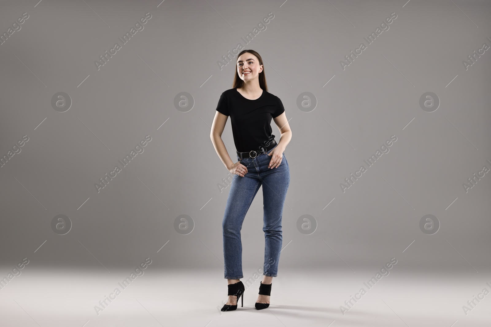 Photo of Smiling woman in stylish jeans on grey background