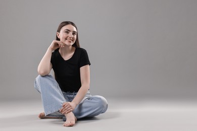 Photo of Smiling woman in stylish jeans on grey background. Space for text