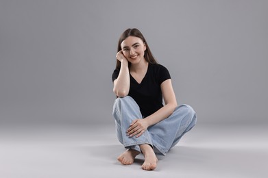 Photo of Smiling woman in stylish jeans on grey background