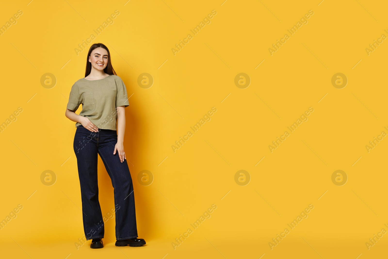 Photo of Smiling woman in stylish jeans on orange background. Space for text