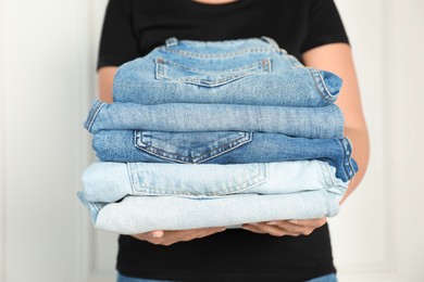 Photo of Woman with stack of different stylish jeans near light wall indoors, closeup