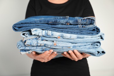 Photo of Woman with stack of different stylish jeans near light wall indoors, closeup