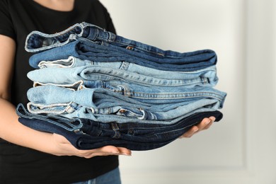 Photo of Woman with stack of different stylish jeans near light wall indoors, closeup