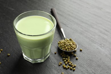 Photo of Fresh mung bean juice in glass and seeds on black table, closeup. Space for text