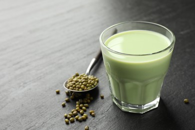 Photo of Fresh mung bean juice in glass and seeds on black table, closeup. Space for text