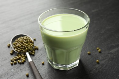 Photo of Fresh mung bean juice in glass and seeds on black table, closeup